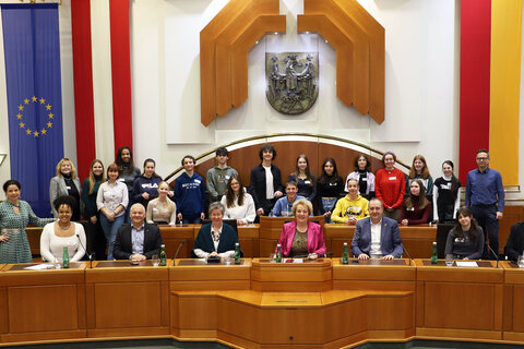 DDr. Barbara Glück (l., stehend) und Landtagspräsidentin Verena Dunst (4.v.r., vorne) sowie Auslandsdiener Jonathan Dorner (2.v.r., vorne) mit Grünen Klubobfrau Mag.a Regina Petrik (3.v.l.), den Landtagsabgeordneten Gerhard Bachmann (2.v.r., vorne) und Gerald Handig (2.v.l., vorne) sowie den Schülerinnen und Schülern der Klasse 7a.